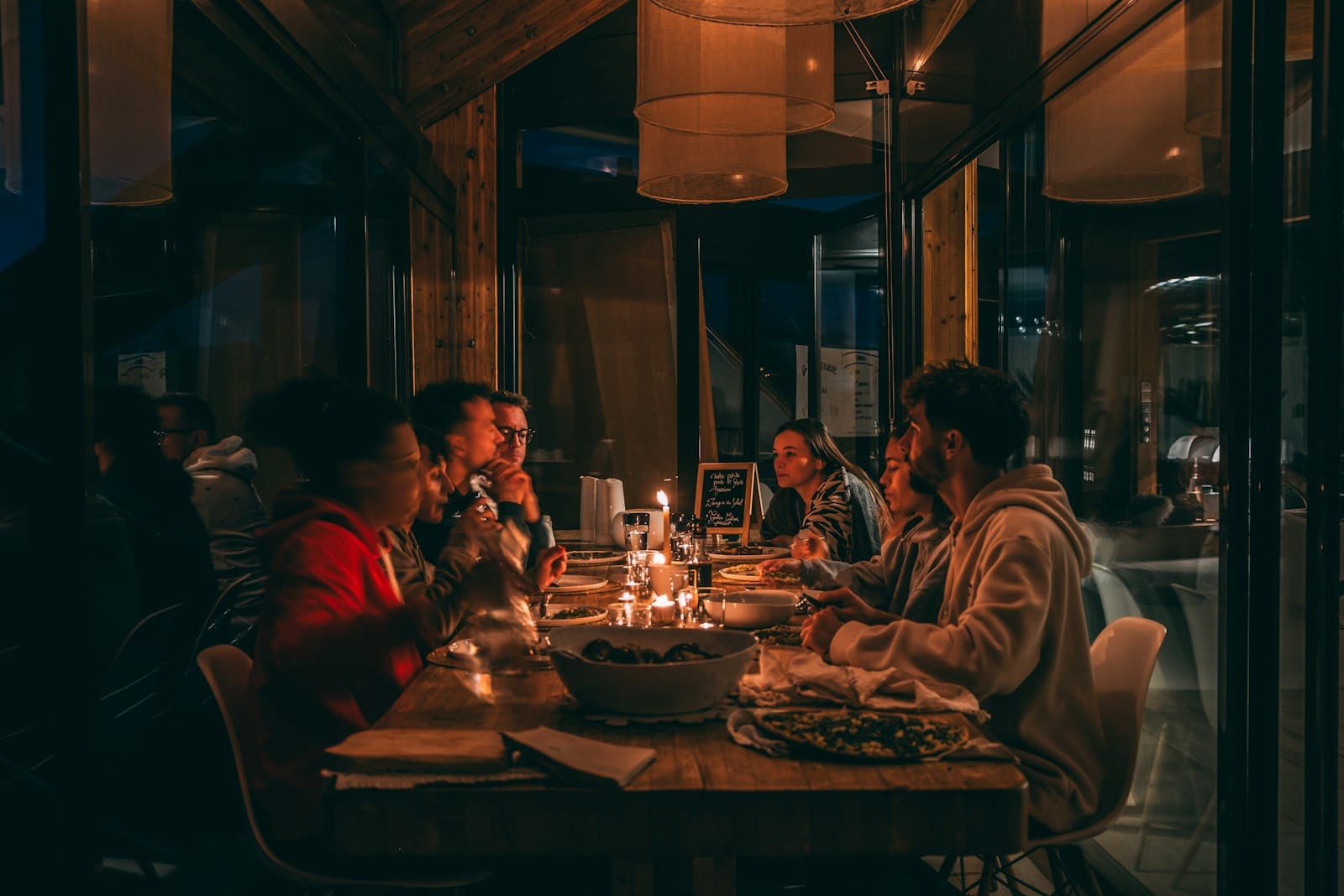 A long candlelit dinner table surrounded by friends at night