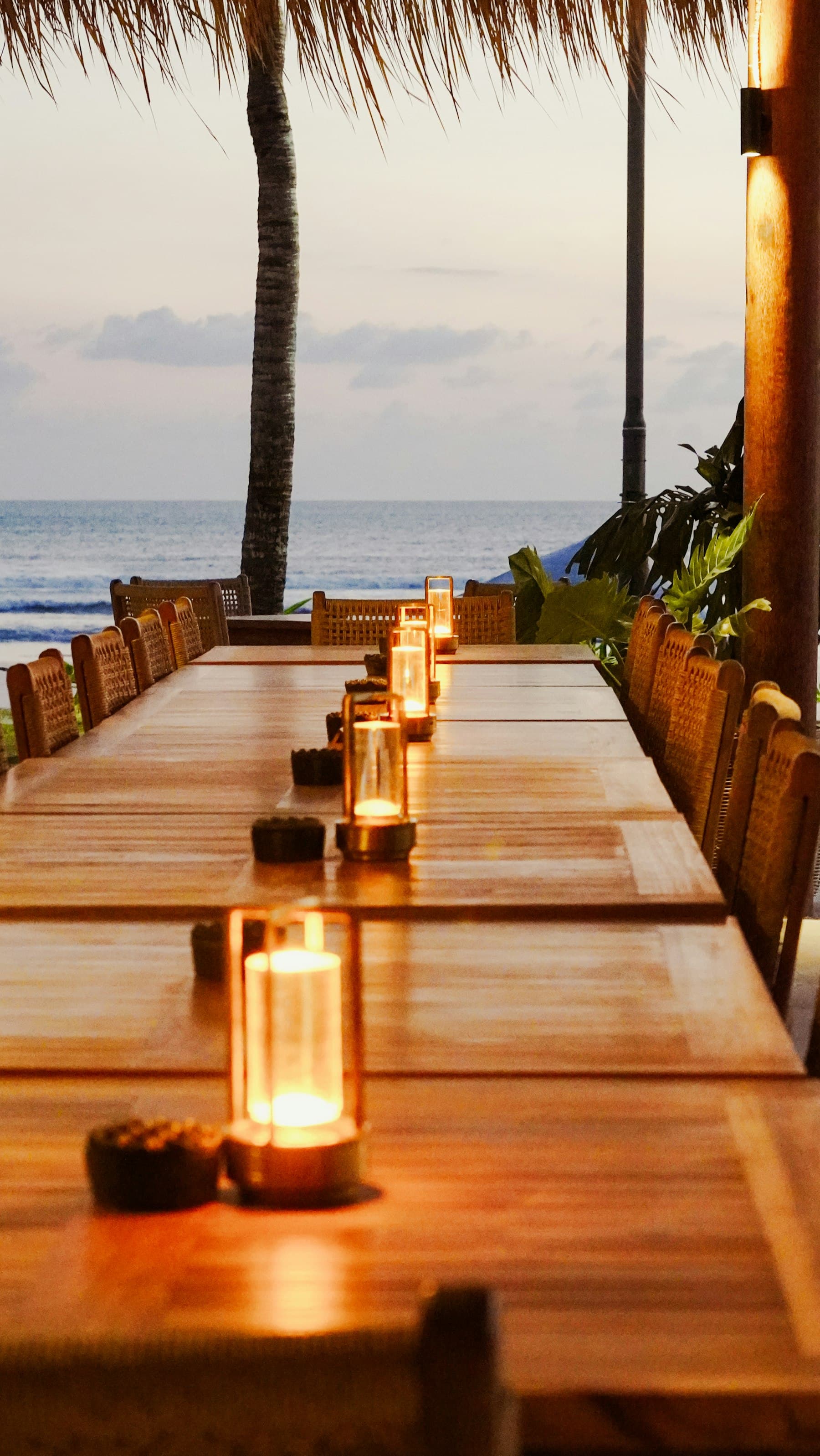 A long candlelit table on a terrace beside the sea at dusk