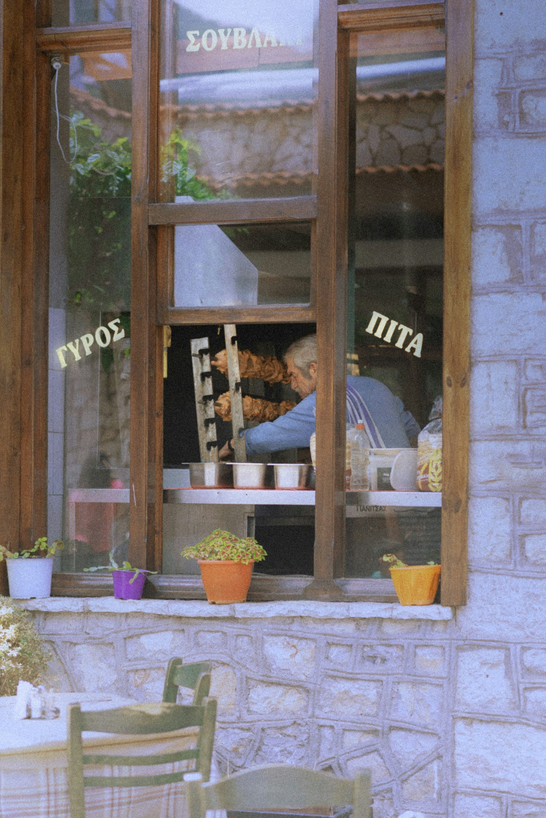 A cook at work behind a taverna window painted with Greek signage